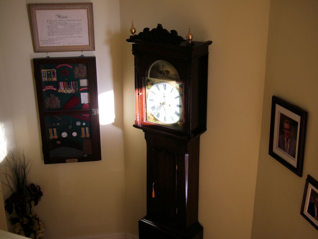 Tall case clock on a landing with morning sun reflecting on the dial